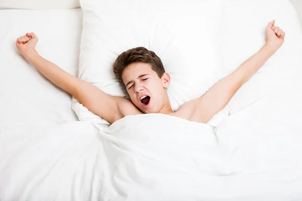Niño dormido acostado en la cama escondiendo la cara bostezante con manta — Foto de Stock