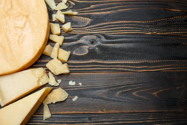 Cabeça de queijo duro parmesão ou parmigiano e pedaços sobre fundo de madeira — Fotografia de Stock