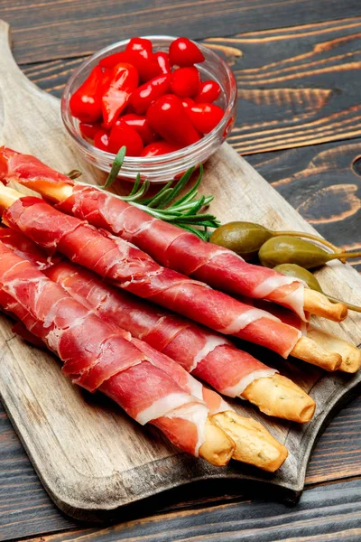 Petisco tradicional italiano presunto crudo paus de pão, pimentas e alcaparras — Fotografia de Stock