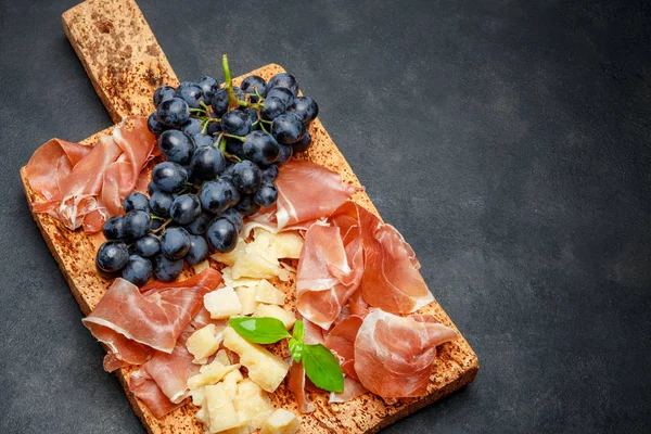 Comida italiana com uvas, presunto e queijo sobre tábua de cortiça — Fotografia de Stock