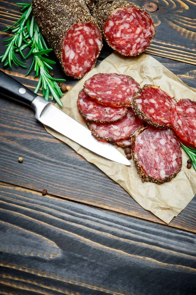 Dried organic salami sausage covered with pepper on wooden background — Stock Photo, Image