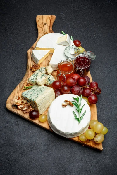 Various types of cheese and jam on wooden cutting board — Stock Photo, Image