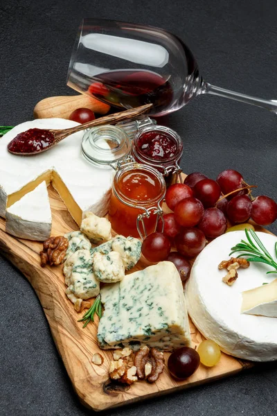 Diverse soorten kaas, jam en wijn op houten snijplank — Stockfoto