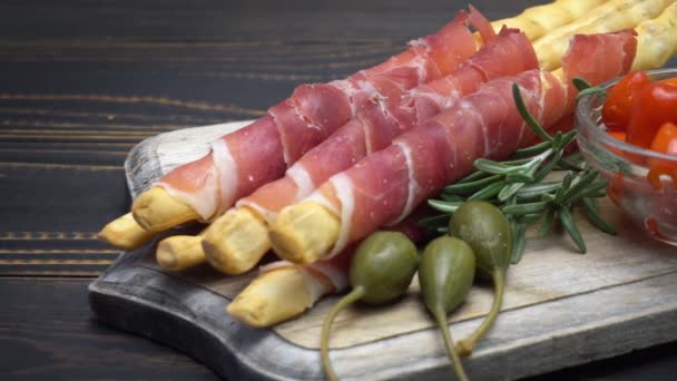 Grissini italiano con jamón, alcaparras y pimienta sobre tabla de cortar de madera — Vídeos de Stock