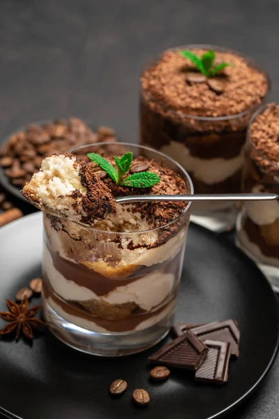 Sobremesa tiramisu clássico em uma xícara de vidro e pedaços de chocolate na placa de corte de pedra no fundo de concreto escuro — Fotografia de Stock