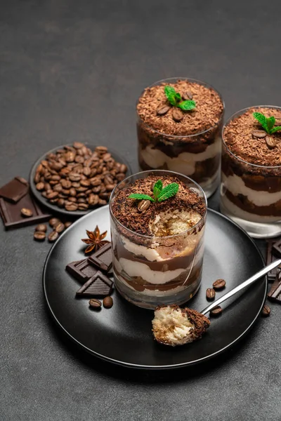 Classic tiramisu dessert in a glass cup and pieces of chocolate on dark concrete background — Stock Photo, Image