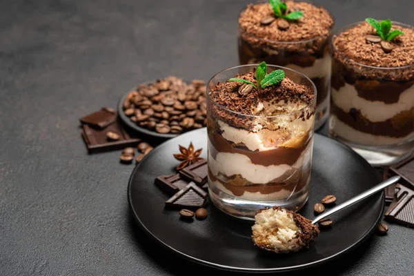 Postre tiramisú clásico en una taza de vidrio y trozos de chocolate sobre fondo de hormigón oscuro — Foto de Stock