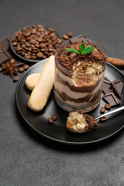 Classic tiramisu dessert in a glass cup and pieces of chocolate on dark concrete background — Stock Photo, Image