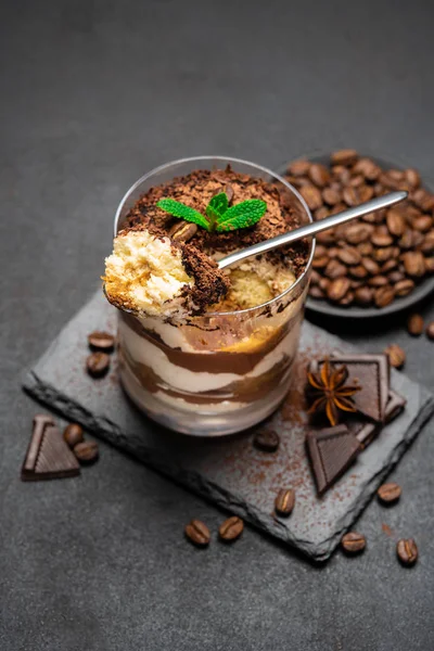 Klassisches Tiramisu-Dessert in einer Glasschale und Schokoladenstücke auf Steinschneidebrett auf dunklem Betongrund — Stockfoto