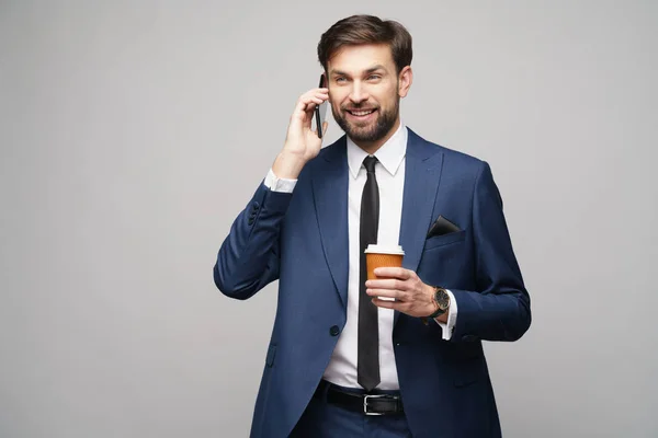 Uomo d'affari che parla al telefono e tiene una tazza di caffè isolata su sfondo grigio — Foto Stock