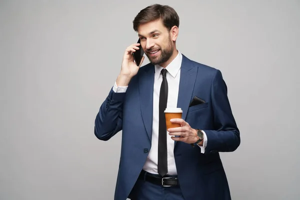 Uomo d'affari che parla al telefono e tiene una tazza di caffè isolata su sfondo grigio — Foto Stock