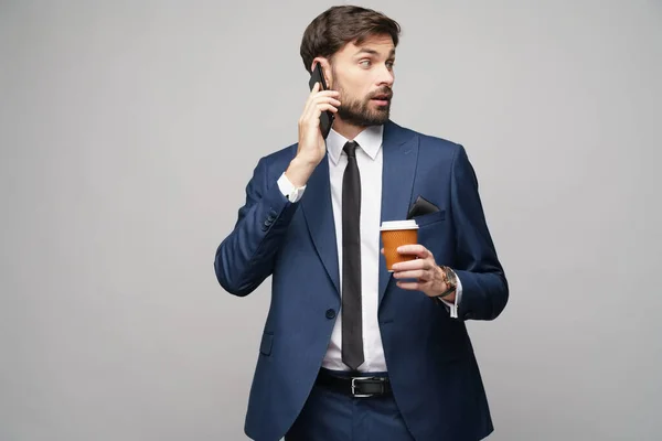 Üzletember beszél a telefonon, és tartja csésze kávé elszigetelt szürke háttér — Stock Fotó