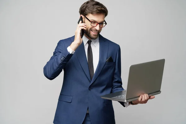 Businessman talking on the phone and holding laptop isolated over grey background — Stock Photo, Image