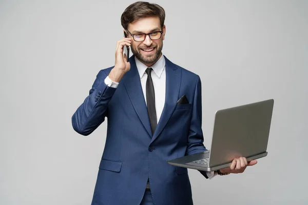 Üzletember beszél a telefonon, és tartsa laptop elszigetelt szürke háttér — Stock Fotó