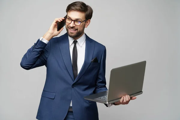 Бизнесмен разговаривает по телефону и держит ноутбук изолирован на сером фоне — стоковое фото