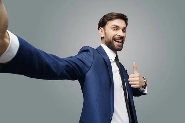 Weitwinkel-Selfie-Aufnahme eines jungen Geschäftsmannes, der auf grauem Hintergrund den Daumen nach oben zeigt — Stockfoto