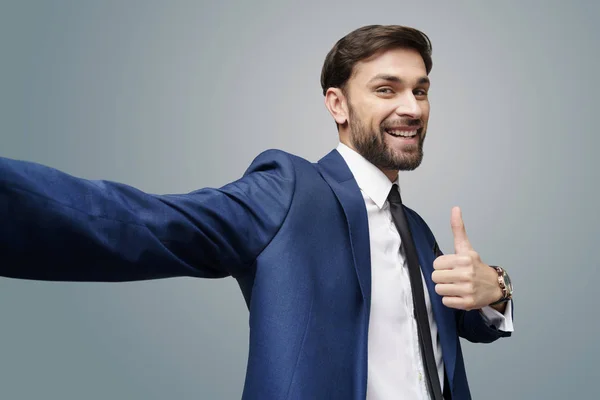 Grande ângulo selfie tiro de jovem homem de negócios indo polegar para cima no fundo cinza — Fotografia de Stock