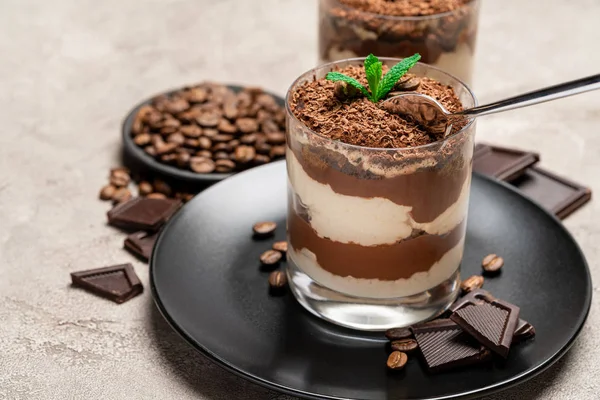 Classic tiramisu dessert in a glass cup and pieces of chocolate on concrete background — Stockfoto