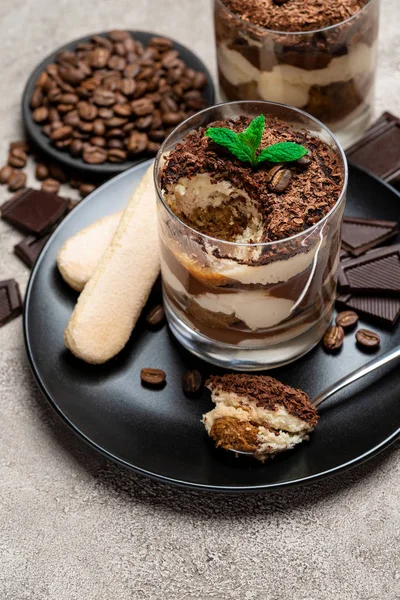 Klassisches Tiramisu-Dessert in einer Glasschale, Schokoladenstücke und savoiardi-Kekse auf Betongrund — Stockfoto