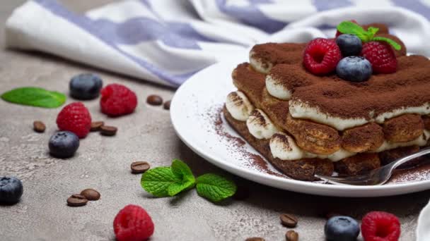 Portion of Classic tiramisu dessert with raspberries and blueberries on grey concrete background — Stock Video