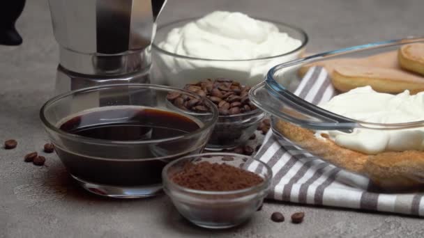 Italian Savoiardi ladyfingers Biscuits and cream in baking dish, coffe maker on concrete background — Stock video