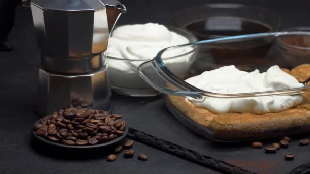 Savoiardi ladyfingers Biscuits and cream in baking dish, coffe maker on dark concrete background — Stockvideo