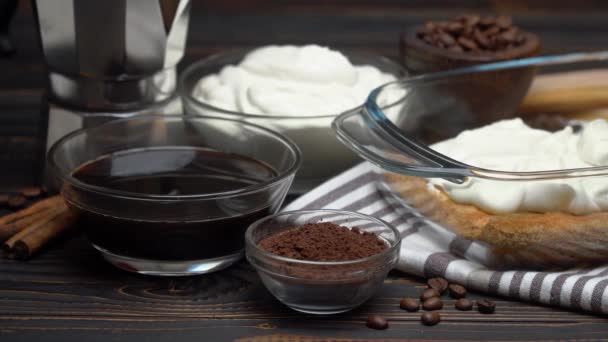 Italian Savoiardi ladyfingers Biscuits and cream in baking dish, coffe maker on wooden background — Stok video