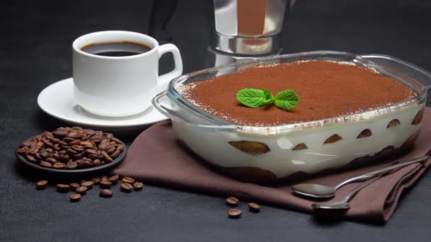 Tiramisu dessert in glass baking dish, cup of espresso and coffee maker on concrete background — Stock Video