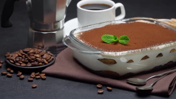 Tiramisu dessert in glazen bakvorm, kopje espresso en koffiezetapparaat op een betonnen ondergrond — Stockvideo