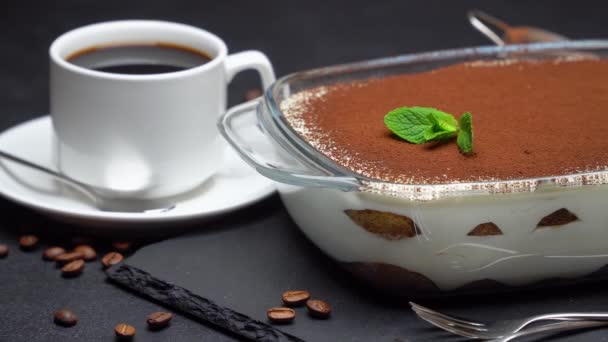 Tiramisu dessert in glass baking dish and cup of fresh hot espresso coffee on concrete background — Stockvideo