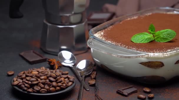 Tiramisu dessert in baking dish, mocha coffee maker and pieces of chocolate on concrete background — Stock Video