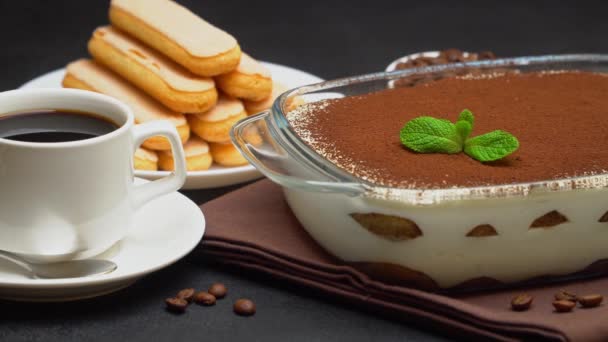Tiramisu dessert in glass baking dish, cup of espresso coffee and savoiardi on concrete background — Stock Video