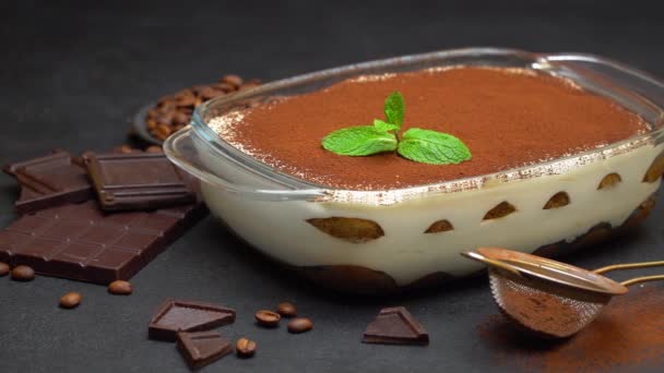 Tiramisu dessert in glass baking dish and pieces of chocolate bar on concrete background — Stock Video
