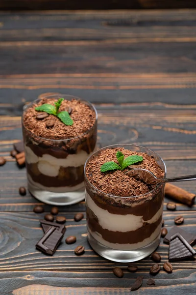 Classico dessert tiramisù in una tazza di vetro e pezzi di cioccolato su sfondo di legno — Foto Stock