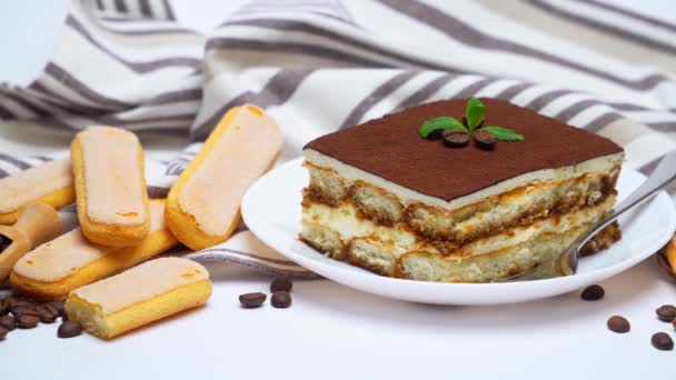 Десерт Тирамису часть на керамической тарелке, печенье savoiardi и кофейных зерен изолированы на белом — стоковое видео