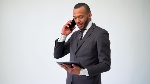 Профессиональный афро-американский бизнесмен держит планшетный компьютер и разговаривает по телефону — стоковое видео