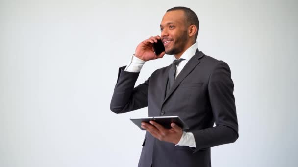 Профессиональный афро-американский бизнесмен держит планшетный компьютер и разговаривает по телефону — стоковое видео