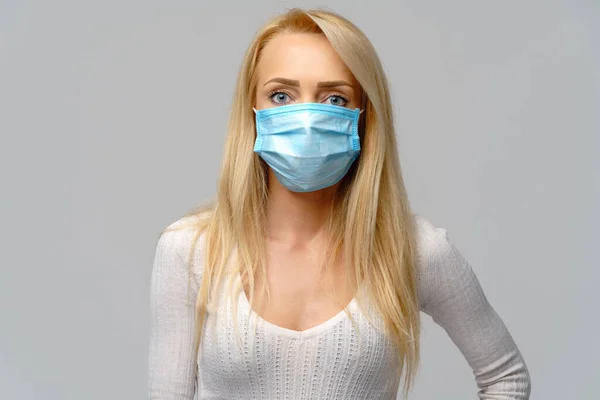 Studio portrait of young woman wearing a face protective mask isolated on gray background - flu virus epidemic protection, dust or pollen allergy, air pollution