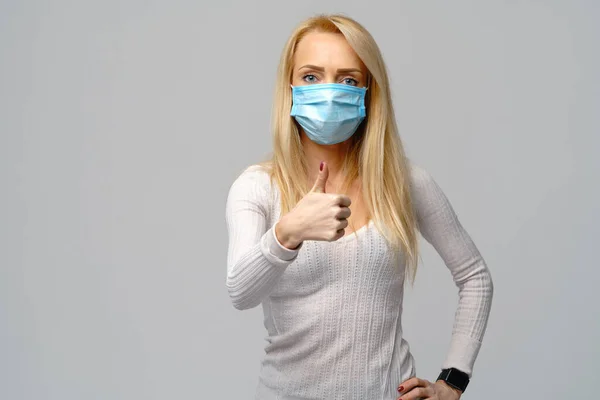 Studio portrait of young woman wearing a face protective mask isolated on gray background - flu virus epidemic protection, dust or pollen allergy, air pollution