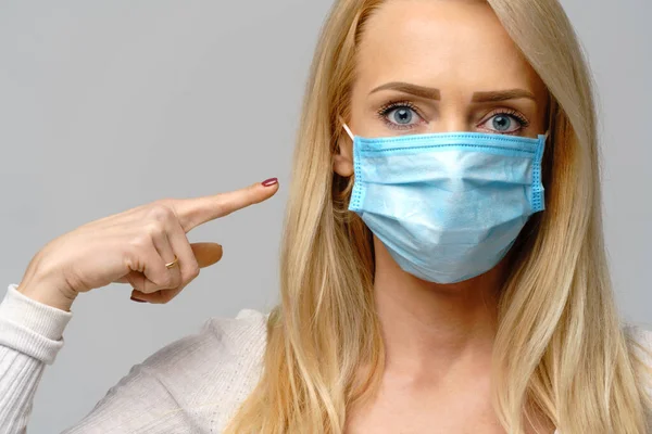 Studio portrait of young woman wearing a face protective mask isolated on gray background - flu virus epidemic protection, dust or pollen allergy, air pollution