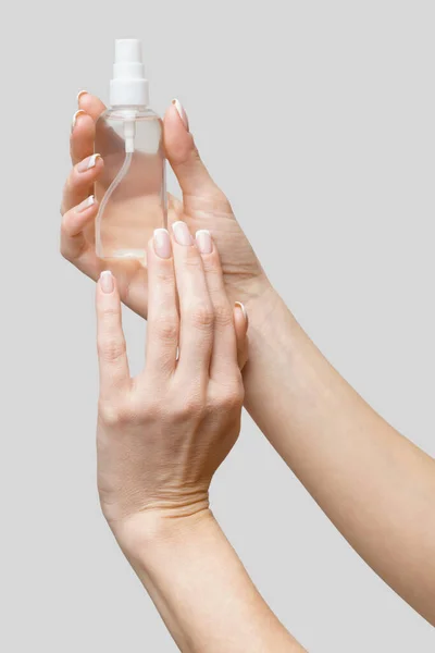 Female hands using hand sanitizer spray dispenser over light grey background — Stock Photo, Image