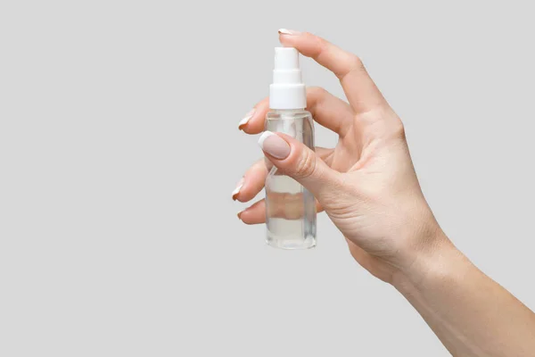 Mani femminili utilizzando erogatore spray disinfettante mano su sfondo grigio chiaro — Foto Stock