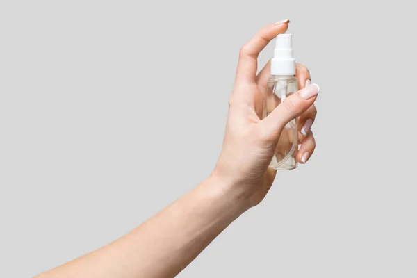 Mani femminili utilizzando erogatore spray disinfettante mano su sfondo grigio chiaro — Foto Stock