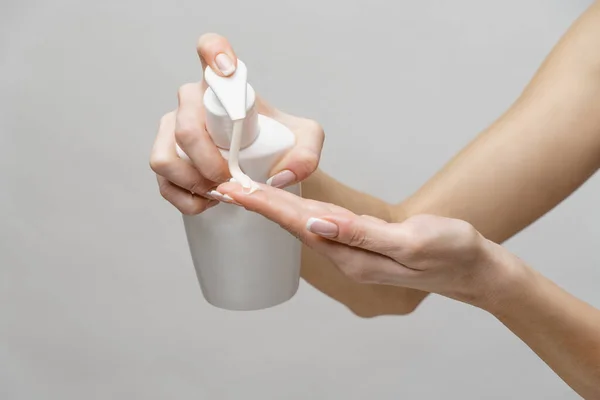 浅灰背景下使用手部清洁剂凝胶或液体肥皂喷雾器的女性手 — 图库照片