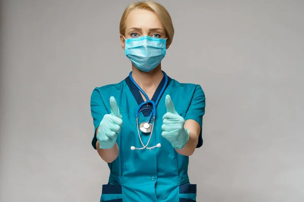 Koruyucu maske takan ve lateks eldiven takan doktor hemşire kadın başparmağını gösteriyor. — Stok fotoğraf