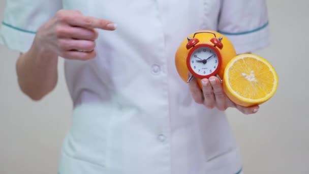 Nutritionist doctor healthy lifestyle concept - holding orange fruit and alarm clock — Stock Video
