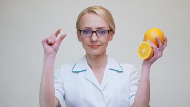 Nutritionist doctor healthy lifestyle concept - holding vitamin pill and orange fruit — Stock Video