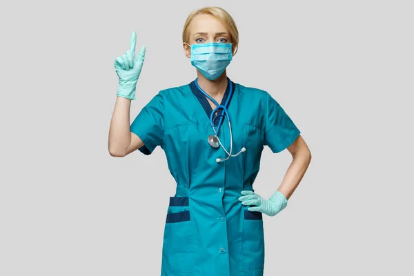Orvosi nővér nő védőmaszkot és latex kesztyűt visel - mutasson ujjal az üres másolótérre — Stock Fotó