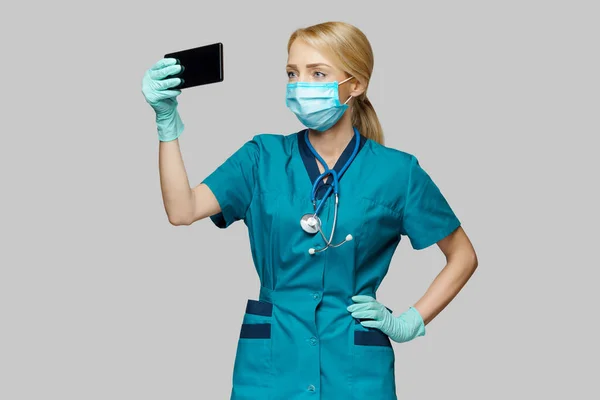 Medical doctor nurse woman wearing protective mask and latex gloves - making video call on the phone Stock Image