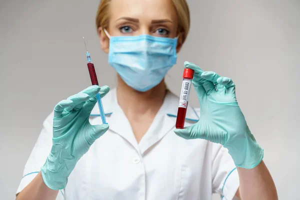 Verpleegkundige vrouw met beschermend masker en handschoenen - met virusbloedtest en injectiespuit — Stockfoto